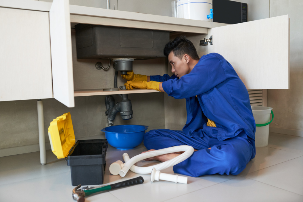 Professional plumber working under a kitchen sink, repairing blocked pipes.